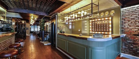 Zona de bar con mostrador de recepción, taburetes de madera y pared de ladrillo.