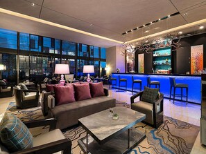 A modern lounge area with a sofa, chairs, a bar, and a large window.