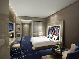Una habitación de hotel moderna con una cama, un escritorio, un televisor y un cuadro abstracto grande.