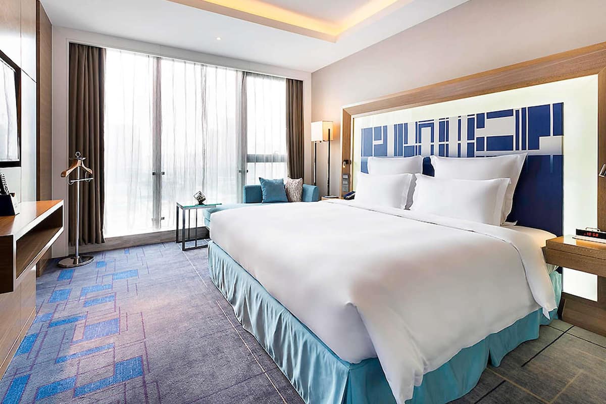 A hotel room with a large bed, a desk, a chair, a nightstand, and a window with curtains.