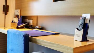 Habitación de hotel con un escritorio de madera, una silla azul, un televisor montado en la pared, una lámpara y un portalápices para el control remoto.