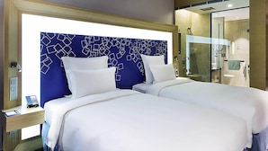 A hotel room with two beds, a blue patterned headboard, a glass shower enclosure, and a bedside table with a phone and notepad. - Novotel Ningbo East (Ningbo)