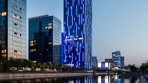 A modern high-rise hotel with a prominent 'NOVOTEL' sign, surrounded by other buildings and a body of water. - Novotel Ningbo East (Ningbo)