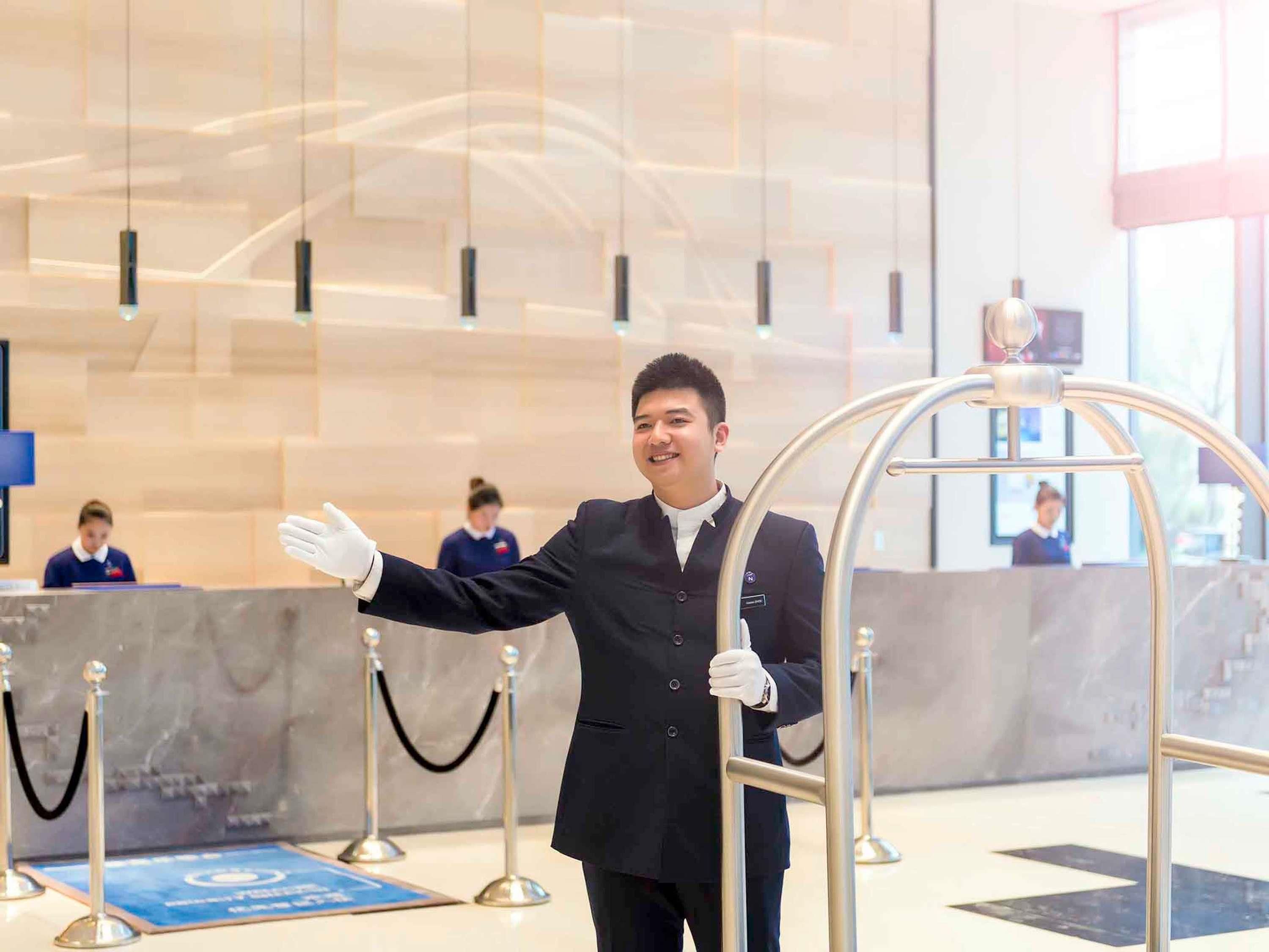 A hotel reception area with a modern design, featuring a reception desk, a glass partition, and a metal barrier with a nameplate.