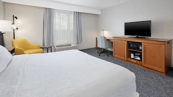 A hotel room with a large bed, a television, a desk with a computer, a chair, and a window with curtains.