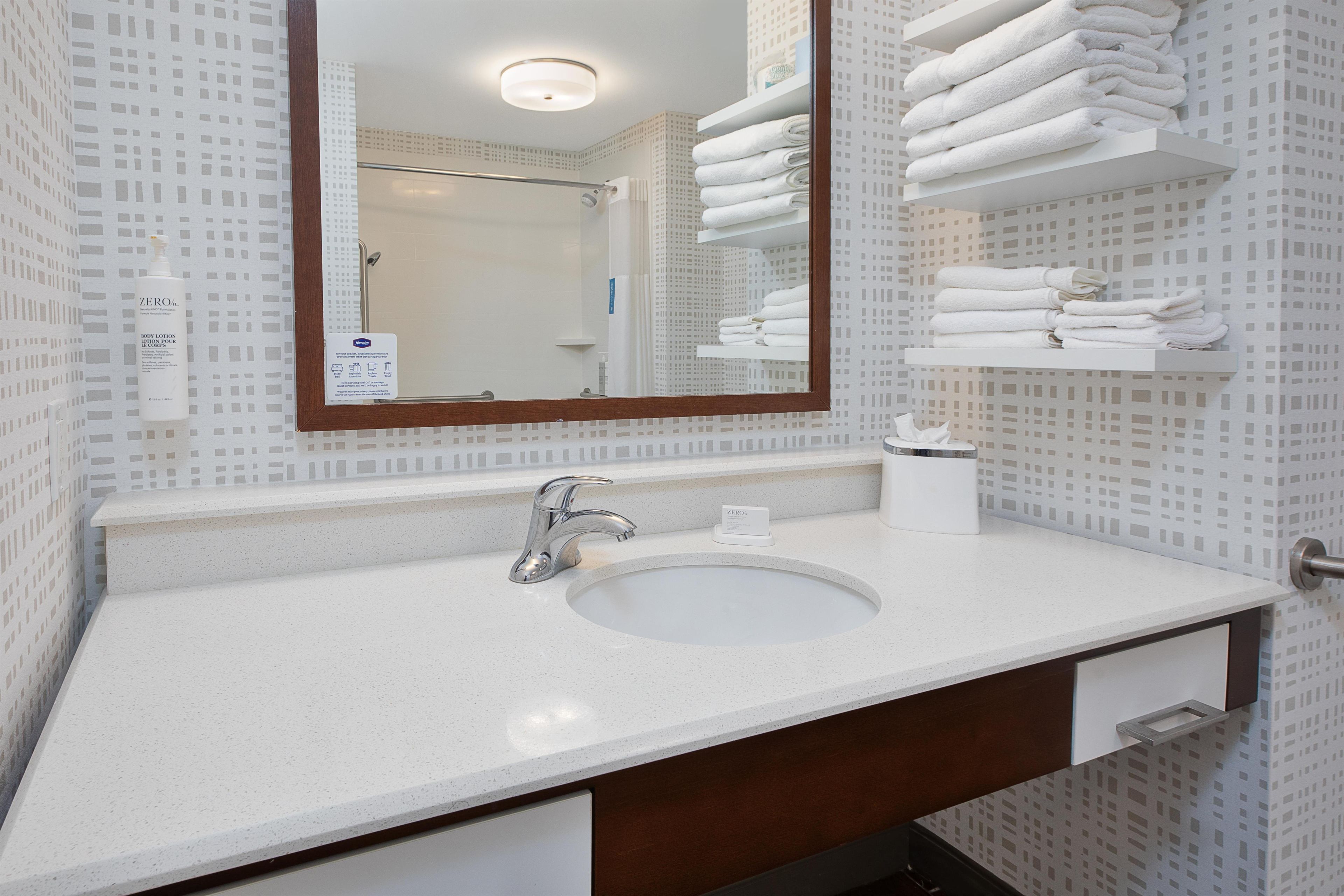 A bathroom with a sink, mirror, towel rack, and a bottle of hand soap.