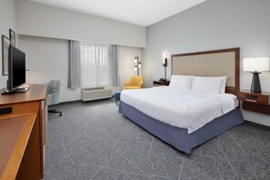 Une chambre d’hôtel équipée d’un lit, d’un bureau, d’une télévision, d’une chaise, d’une lampe et d’une fenêtre avec des rideaux.