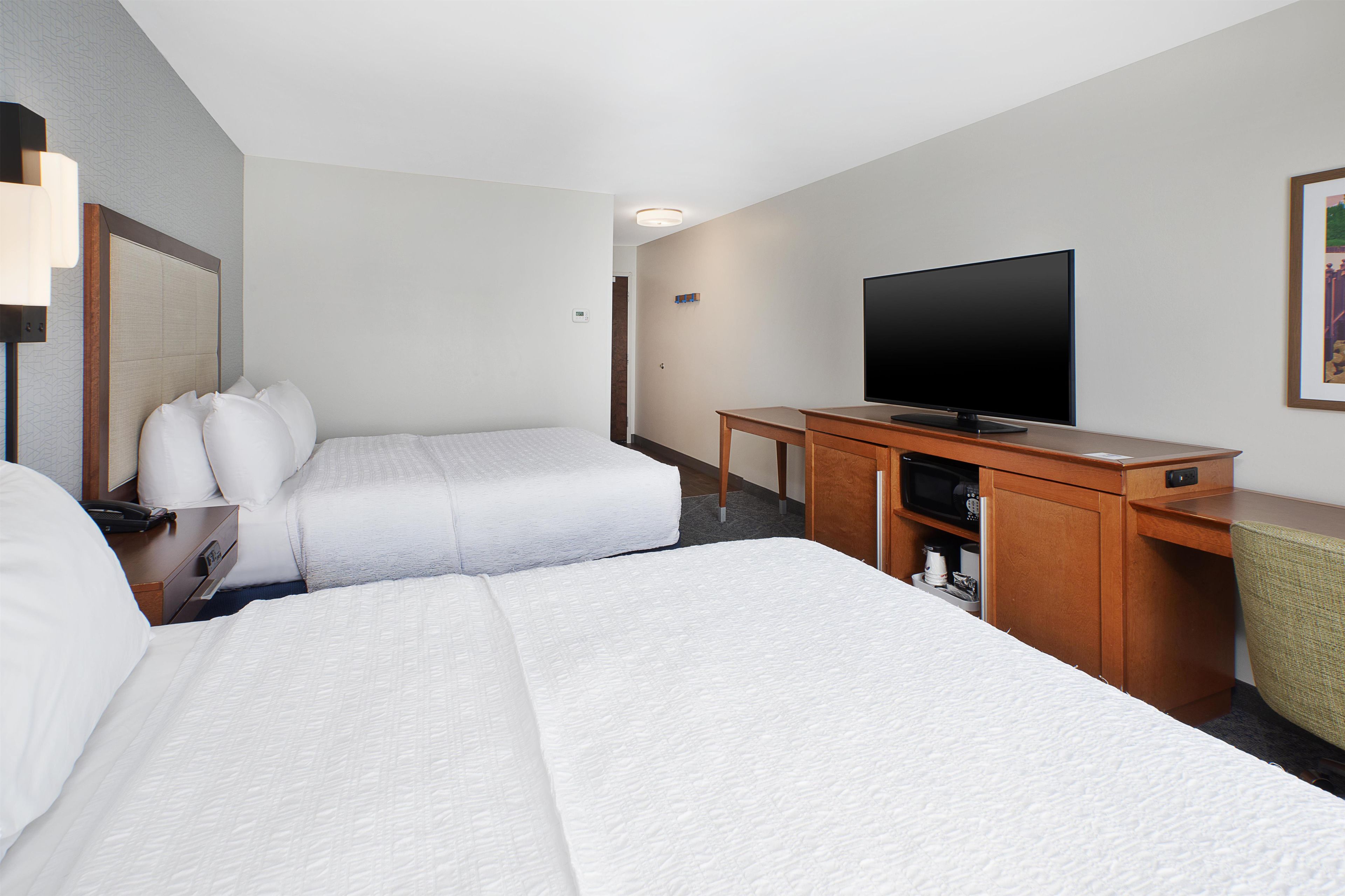 A hotel room with two beds, a television, a desk, and a chair.
