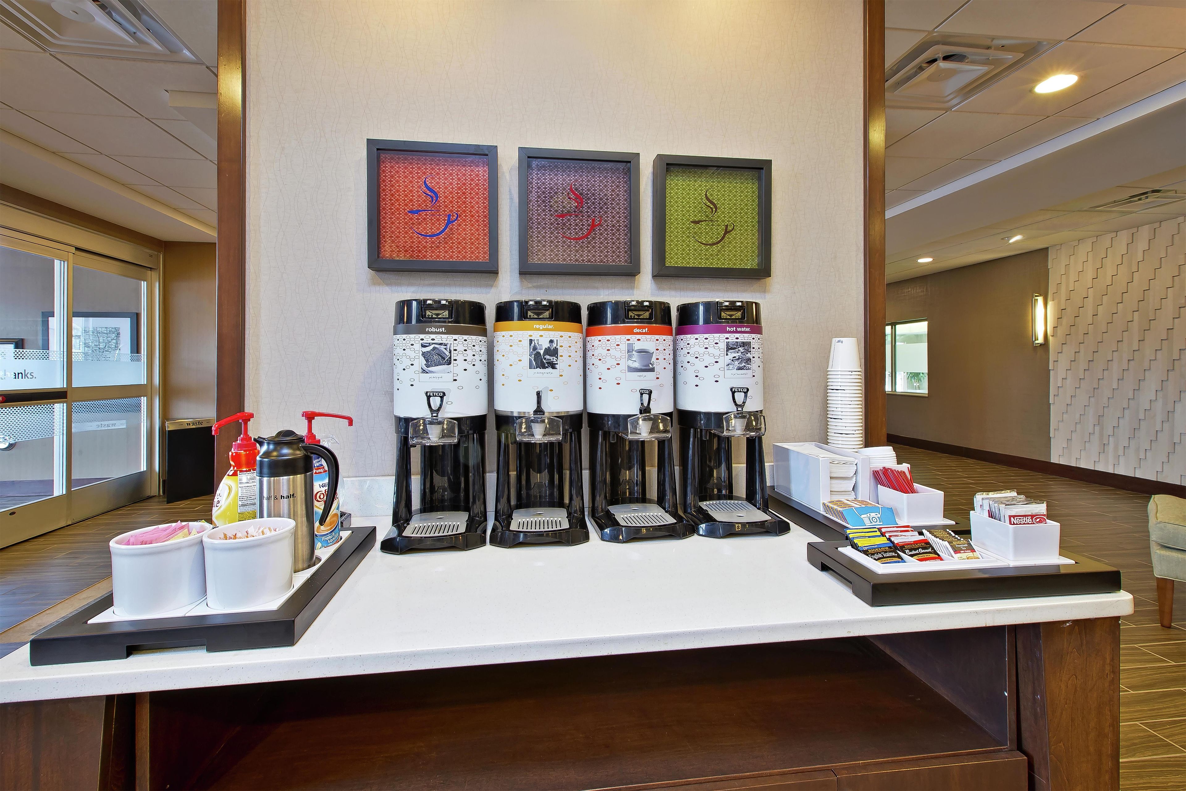 Un espace dédié au café, équipé de quatre distributeurs, de distributeurs d’assaisonnements et d’un plateau contenant des tasses et des condiments.
