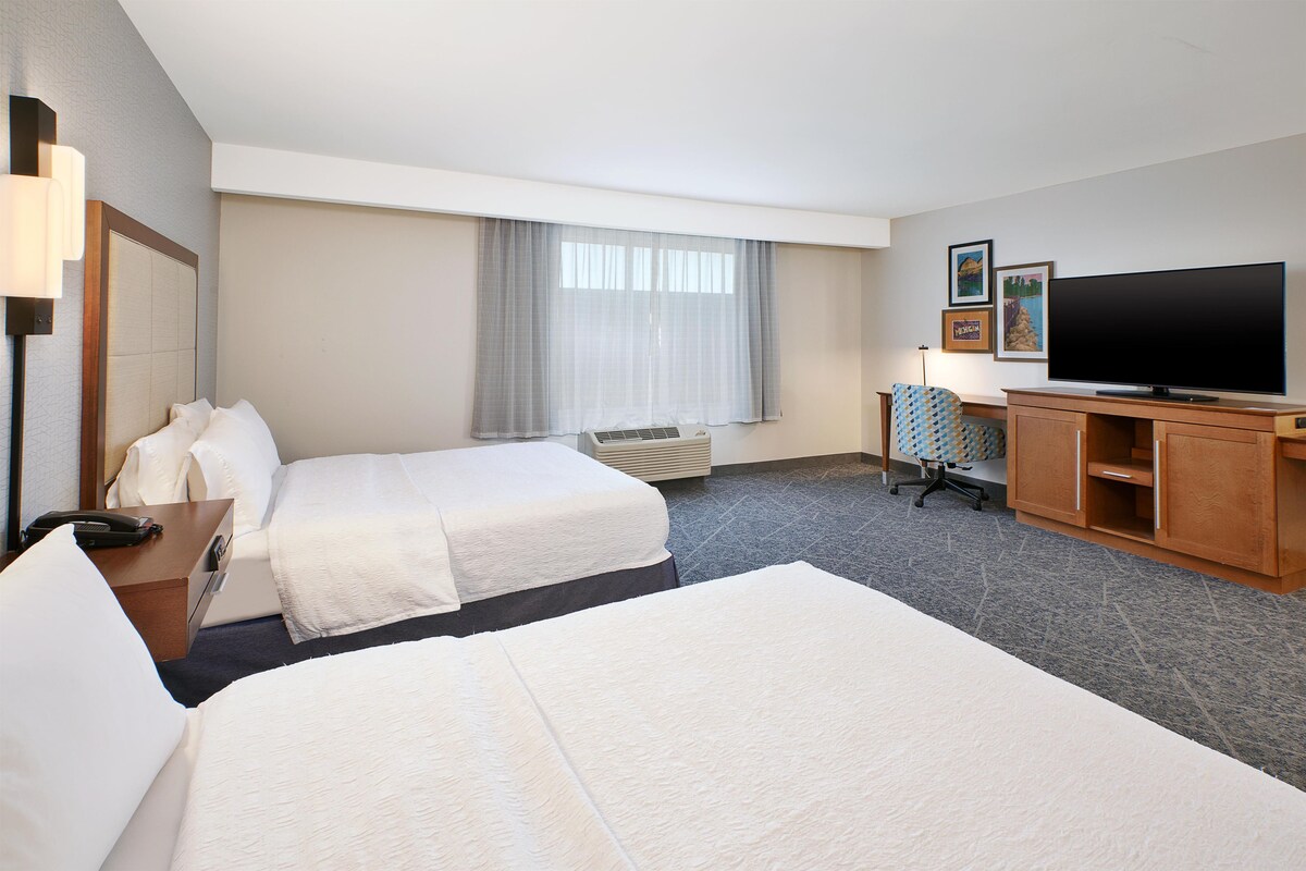 Une chambre d’hôtel avec deux lits, un bureau avec un téléphone, une télévision et une chaise.