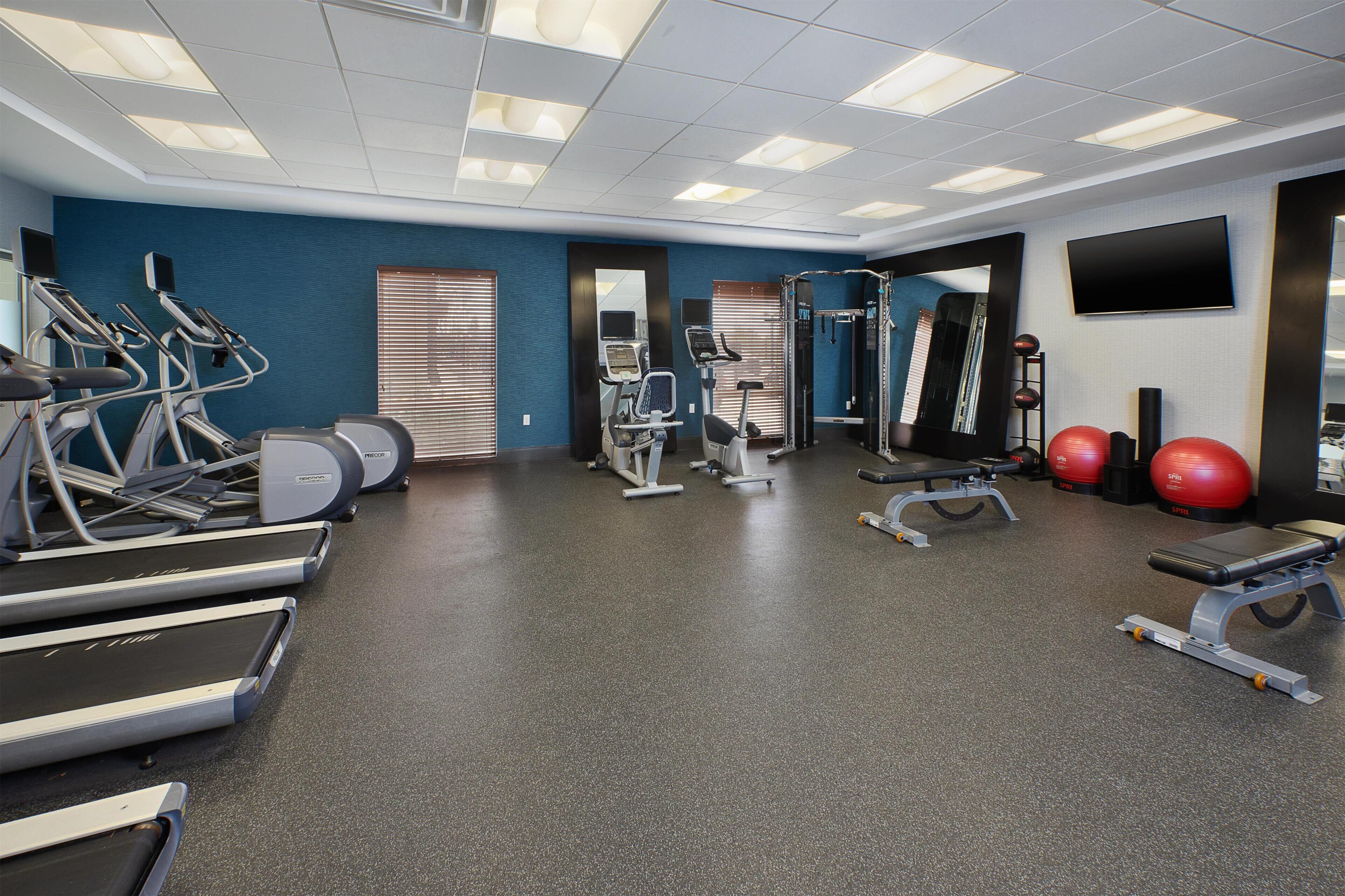 A gym with treadmills, elliptical machines, weight benches, and exercise balls.
