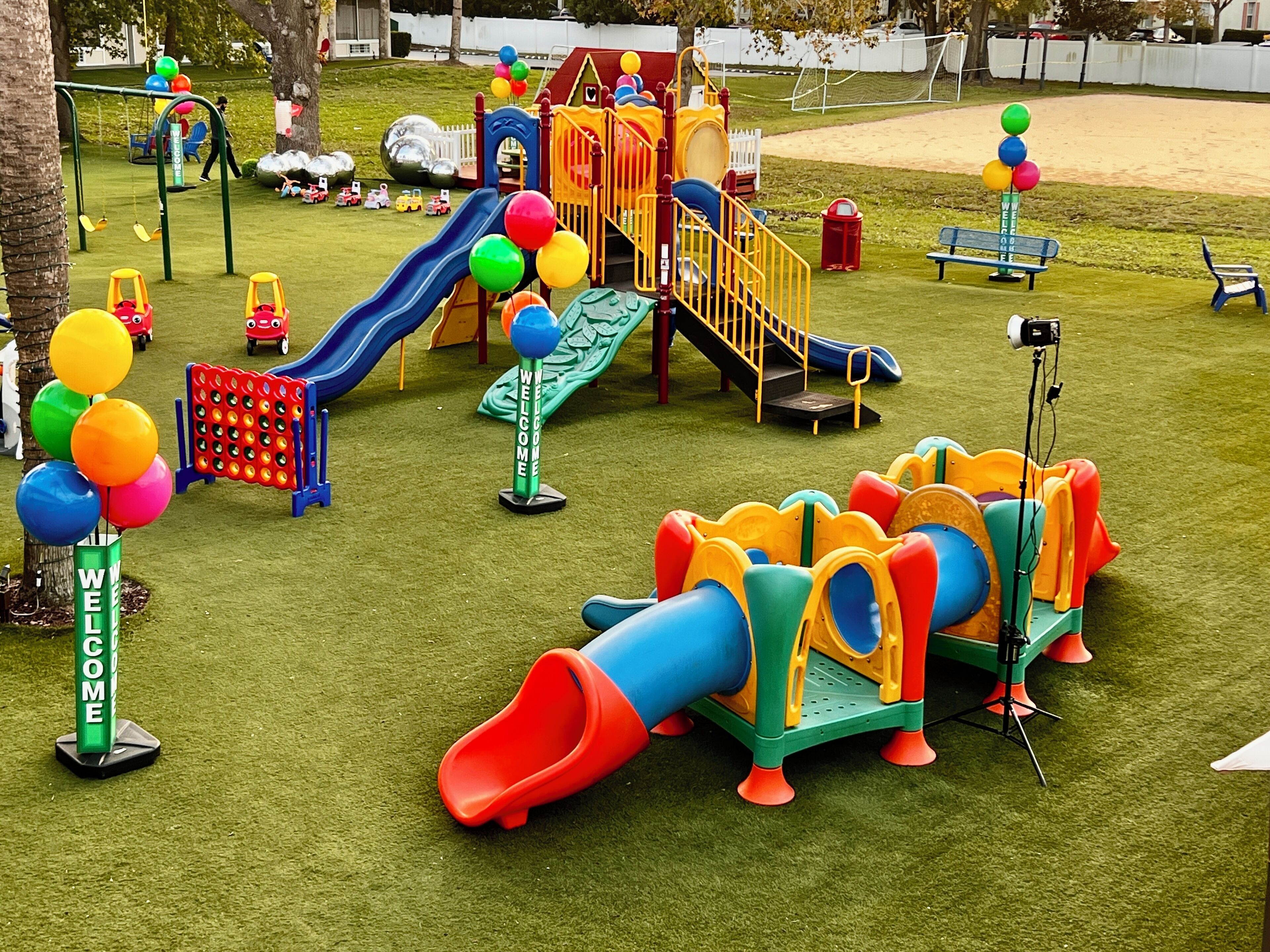 A playground with slides, climbing structures, and a 'Welcome' sign.