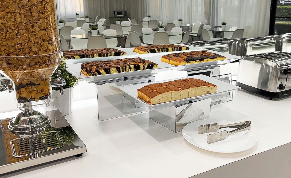 A buffet setup with various desserts on trays, a coffee dispenser, and a toaster.