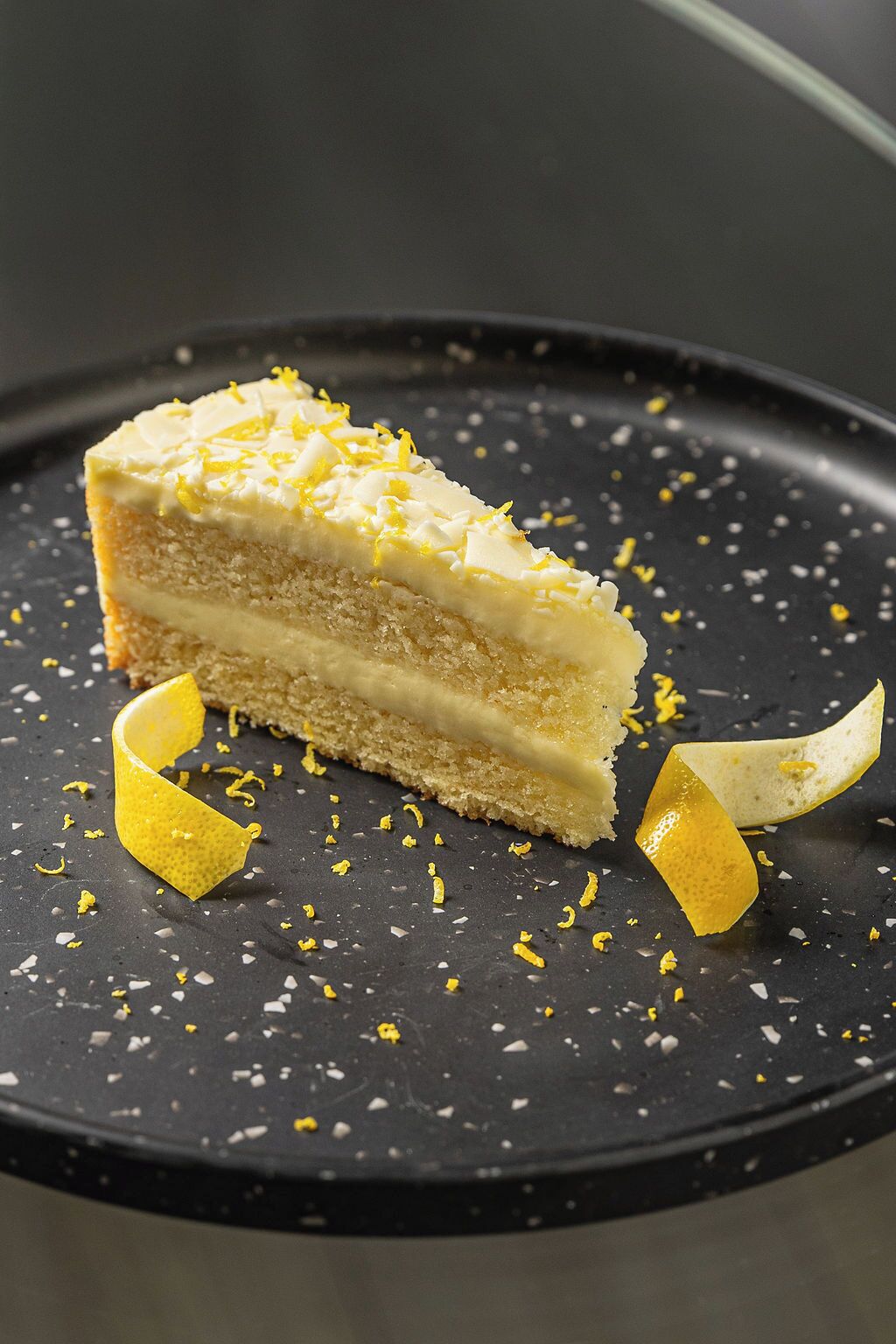 A slice of cake with lemon zest on a dark plate.