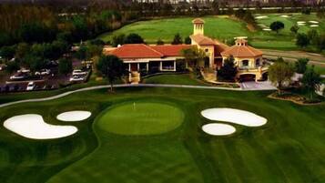 A golf course with a clubhouse featuring a red roof and a tower. There are multiple sand bunkers and a well-maintained lawn.