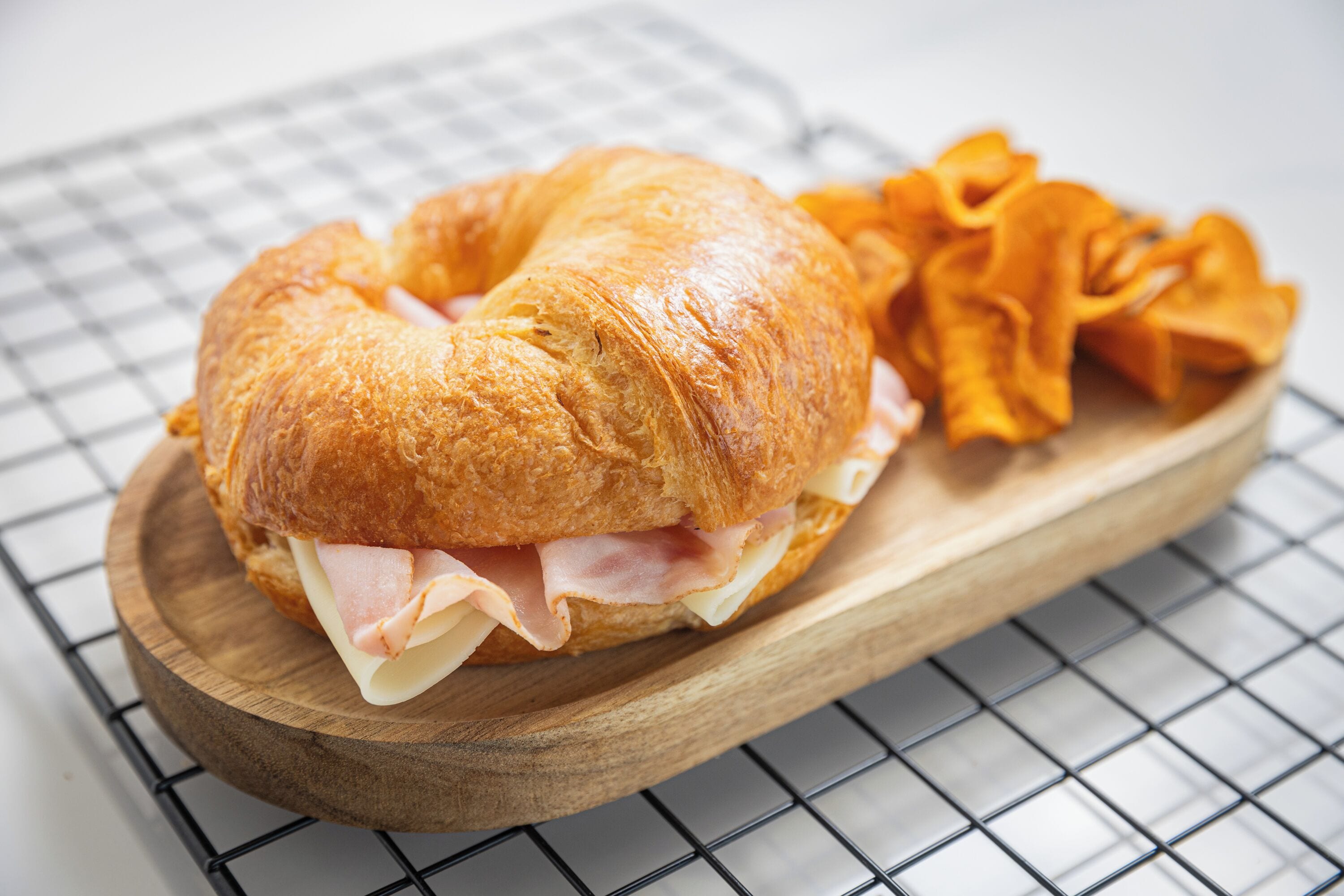 Un sándwich sobre una tabla de madera, con una rejilla metálica al fondo.