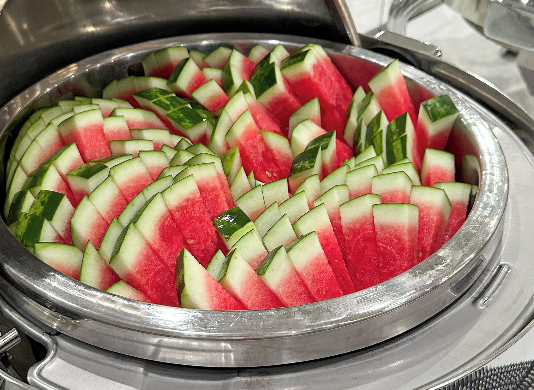 Un grand récipient en métal rempli de tranches de pastèque et de concombre, disposées avec soin.