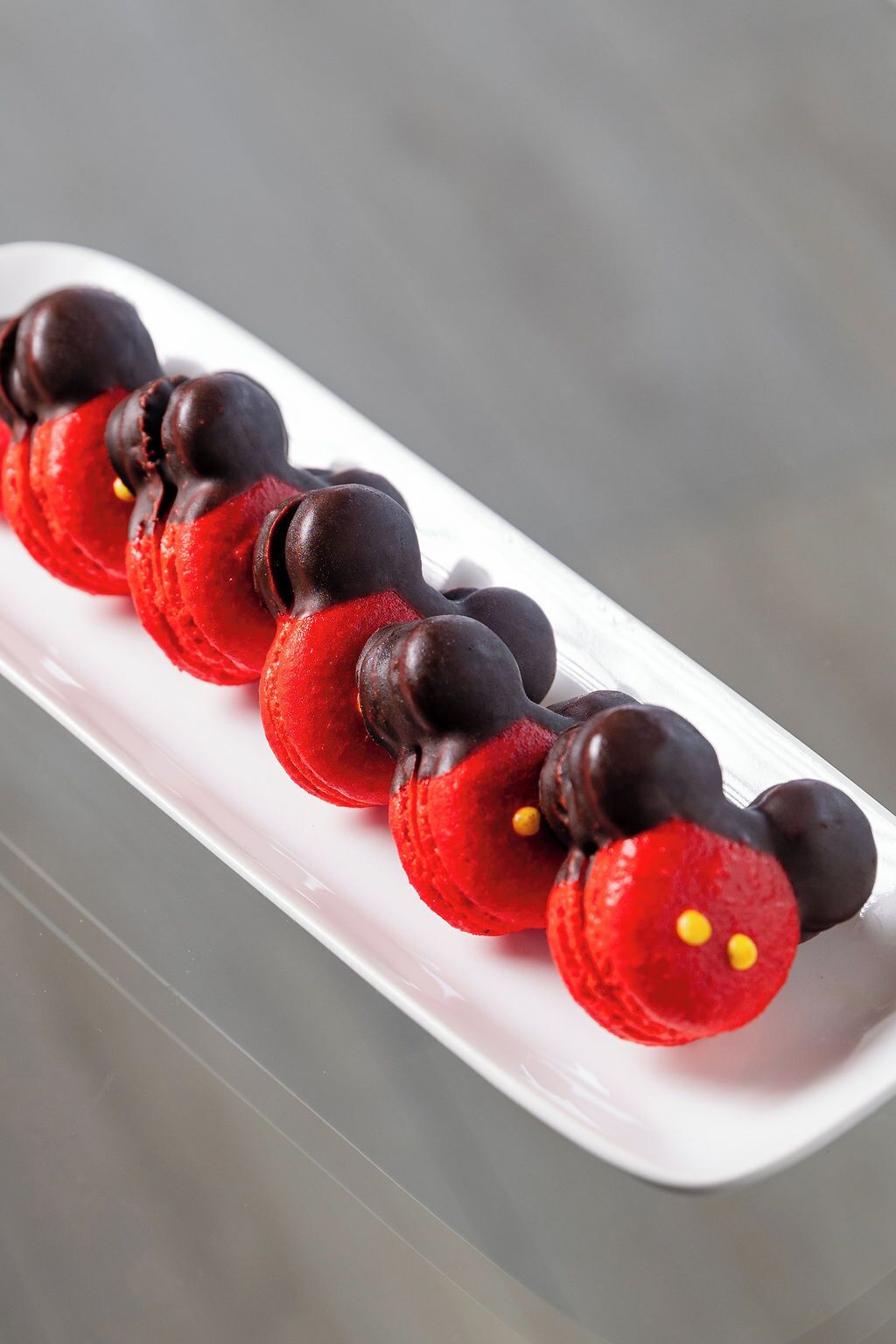 A white rectangular plate with a row of red and chocolate-covered macarons.
