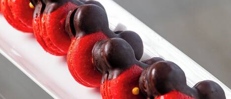 A white rectangular plate with a row of red and chocolate-covered macarons.