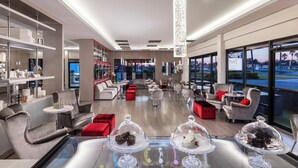Una hall d'albergo moderna con un'ampia disposizione, un'area salotto centrale e grandi finestre che offrono vista sulla città.