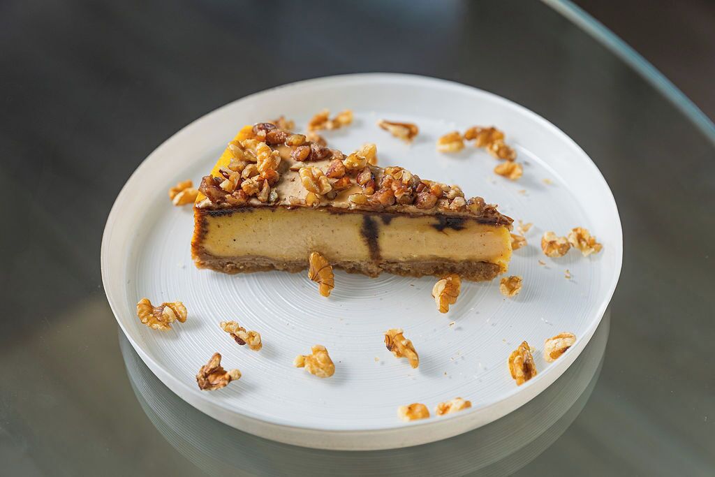 Uma fatia de cheesecake em um prato branco com nozes por cima.