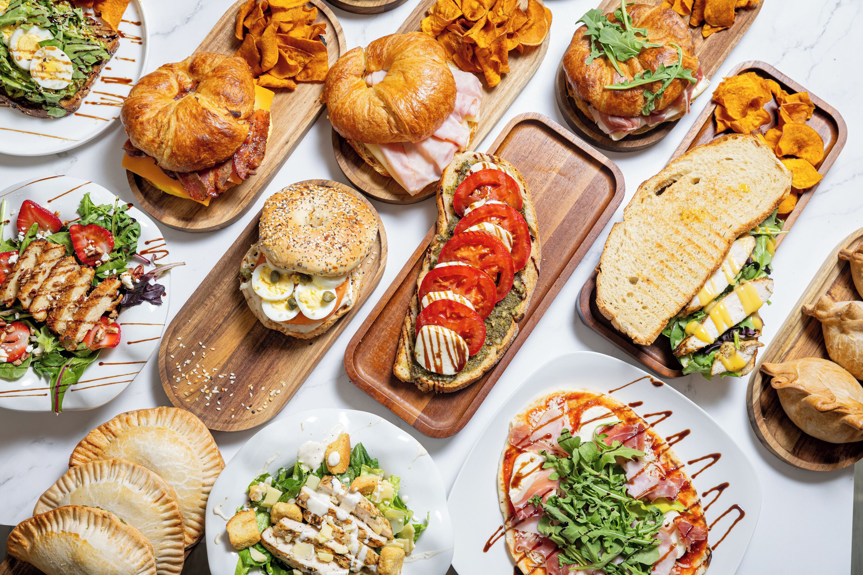 A variety of sandwiches, salads, and pastries on a marble countertop.