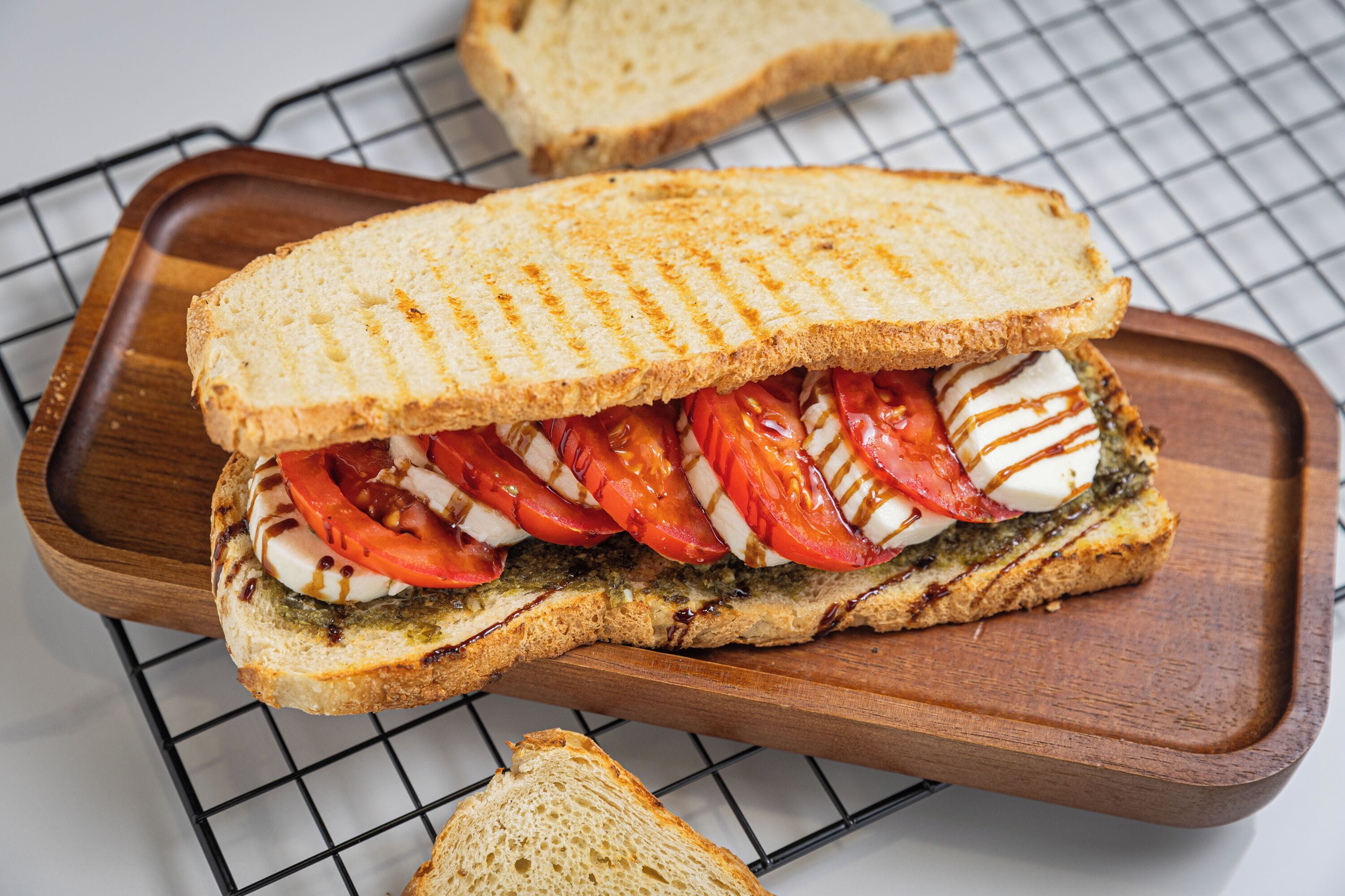 A grilled sandwich with tomato, mozzarella, and pesto on a wooden board.