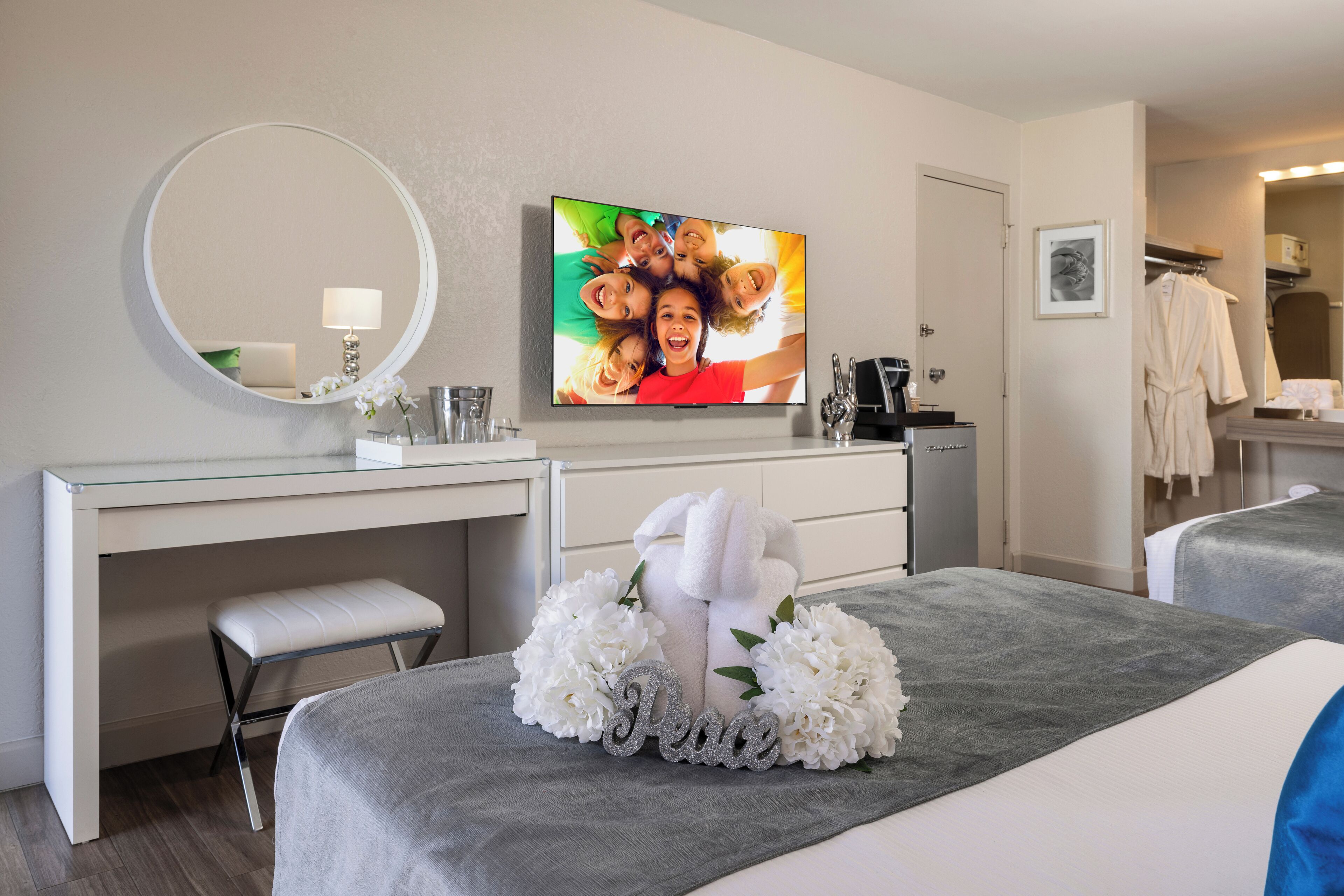 A hotel room with a bed, a desk, a chair, a TV, a mirror, a robe, and a towel.
