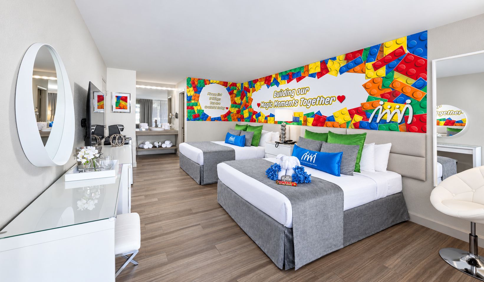 Een moderne hotelkamer met een groot bed, twee nachtkastjes, een spiegel en een kleurrijke wanddecoratie.