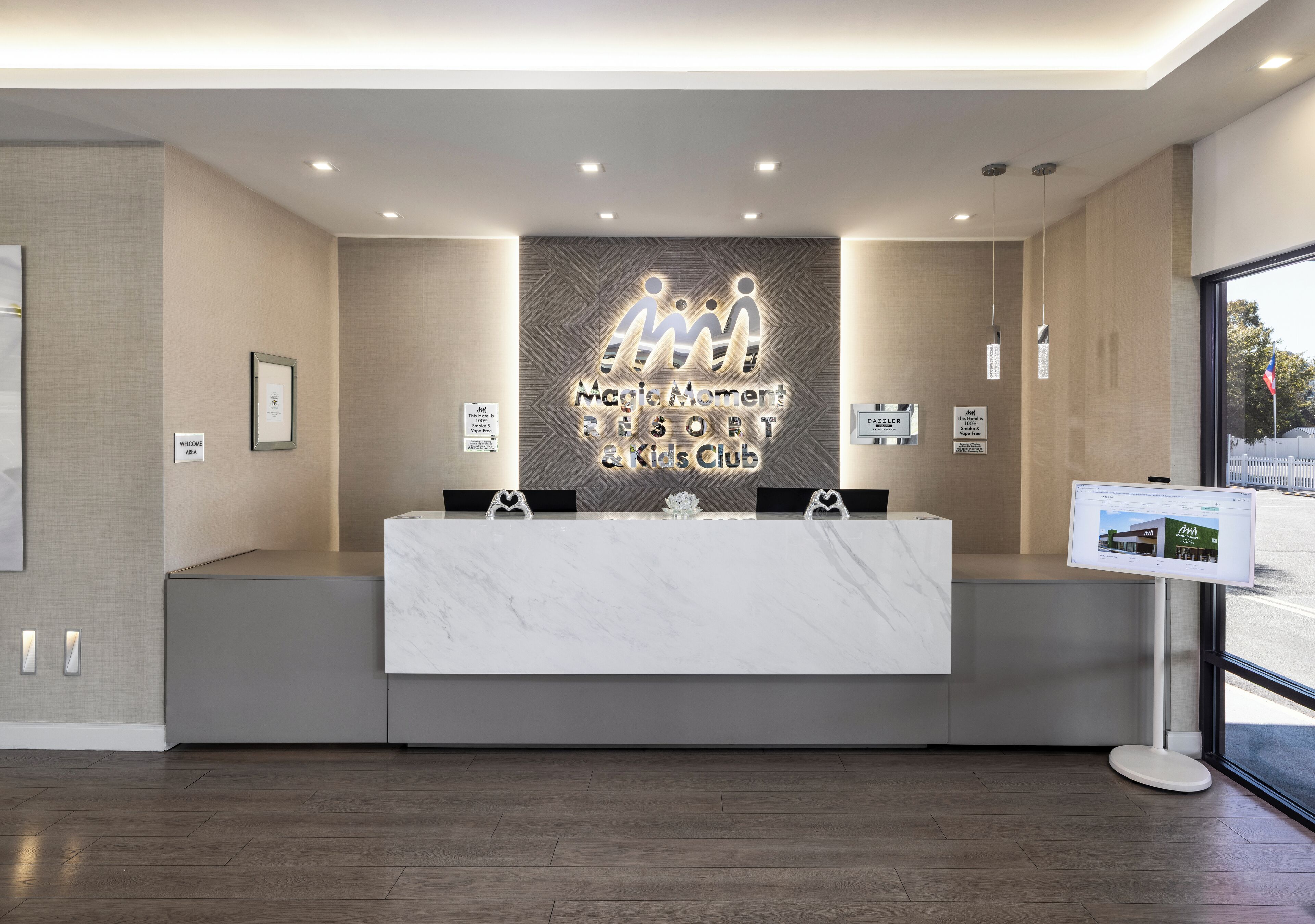 A reception area with a marble counter, a neon sign for Magic Moment Resort & Kids Club, and a digital screen on the right.