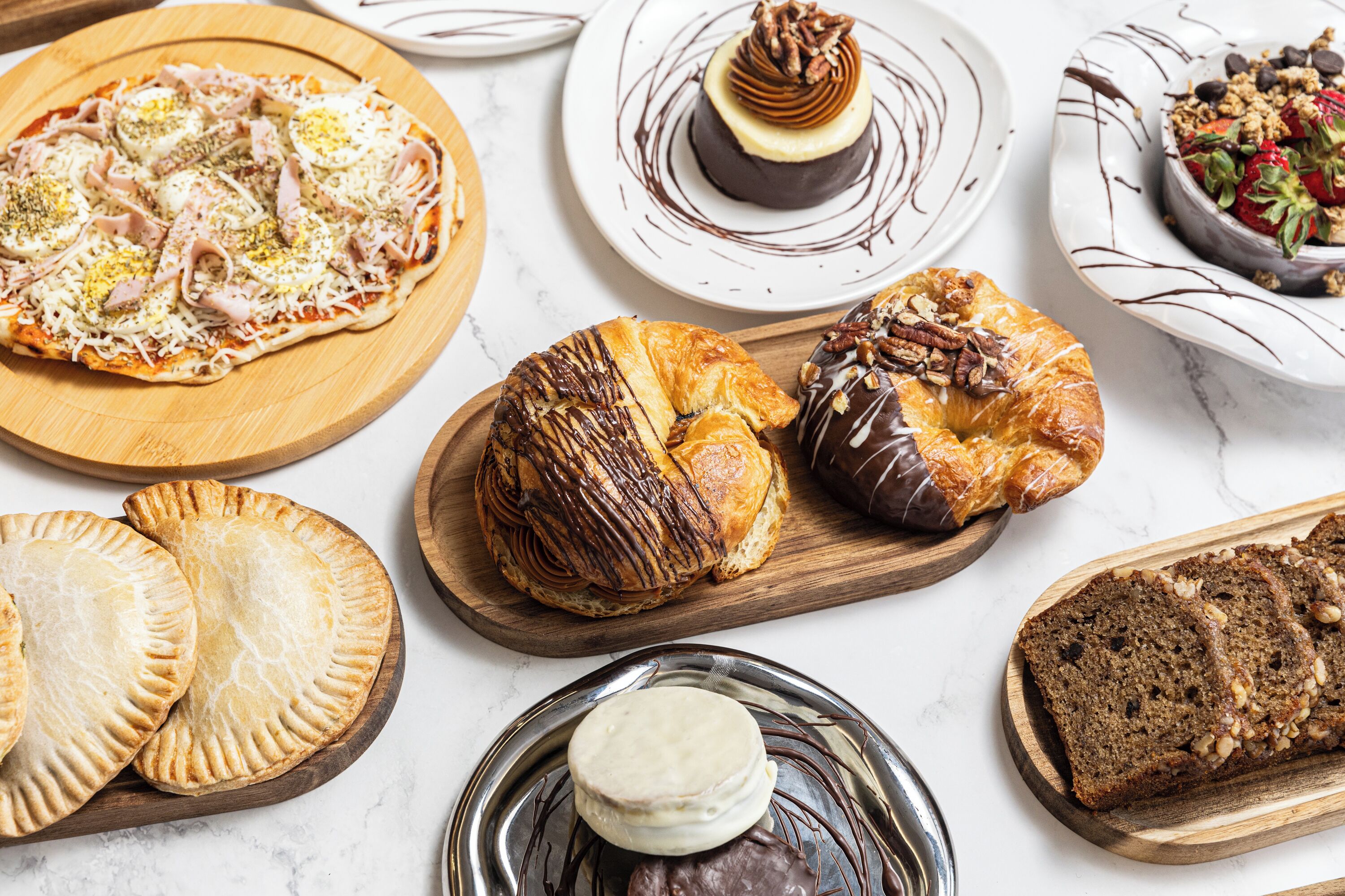 Variedad de productos horneados, incluyendo pizza, pasteles y un postre de chocolate, sobre tablas de madera.