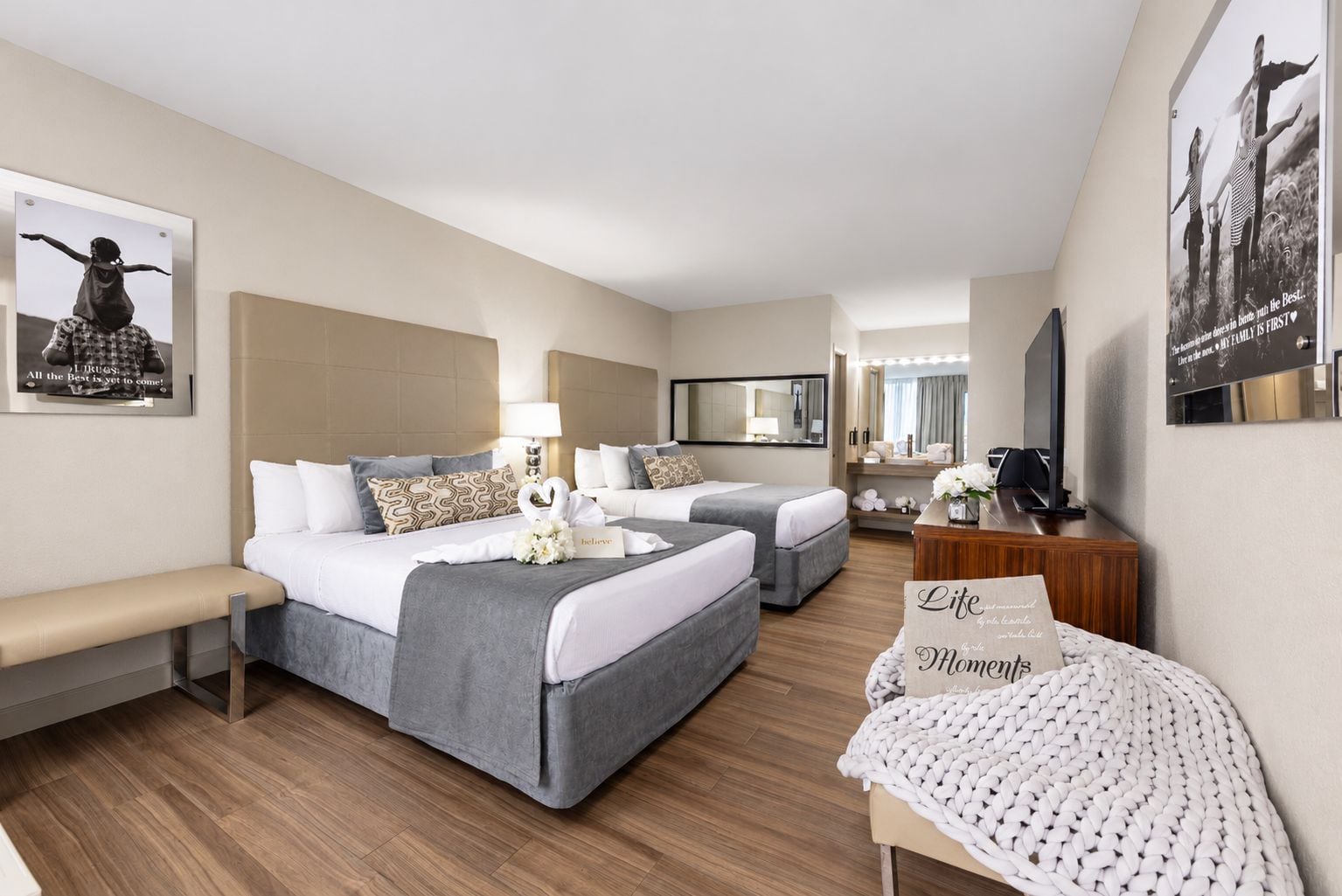 A hotel room with two beds, a bench, a desk, and a mirror.