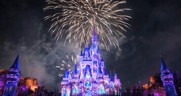 A castle illuminated with blue and purple lights, surrounded by fireworks.