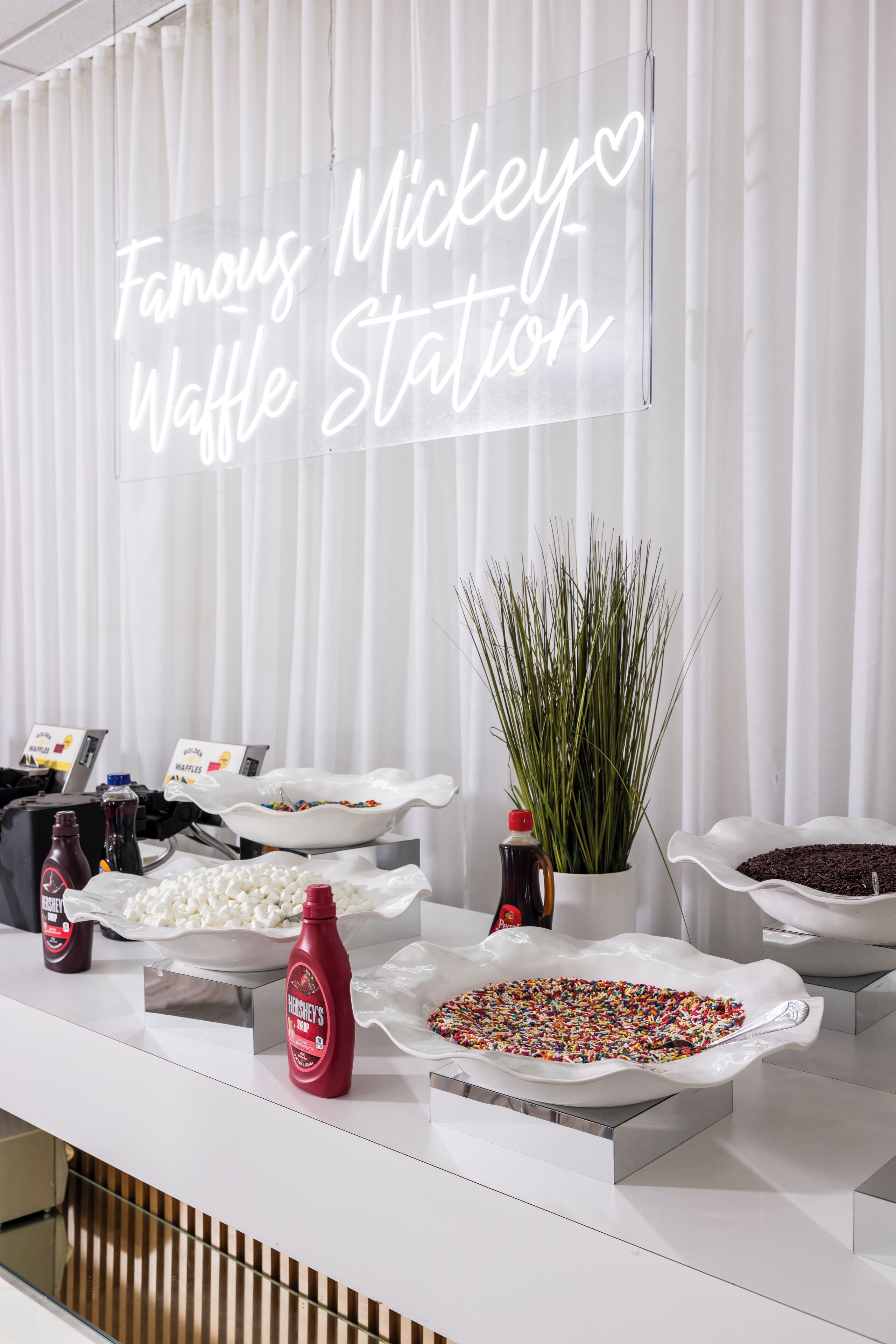 A food station with various toppings and a neon sign reading "Famous Mickey Waffle Station".
