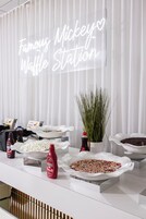 Uma estação de comida com diversos acompanhamentos e um letreiro de neon com a inscrição "Famous Mickey Waffle Station".
