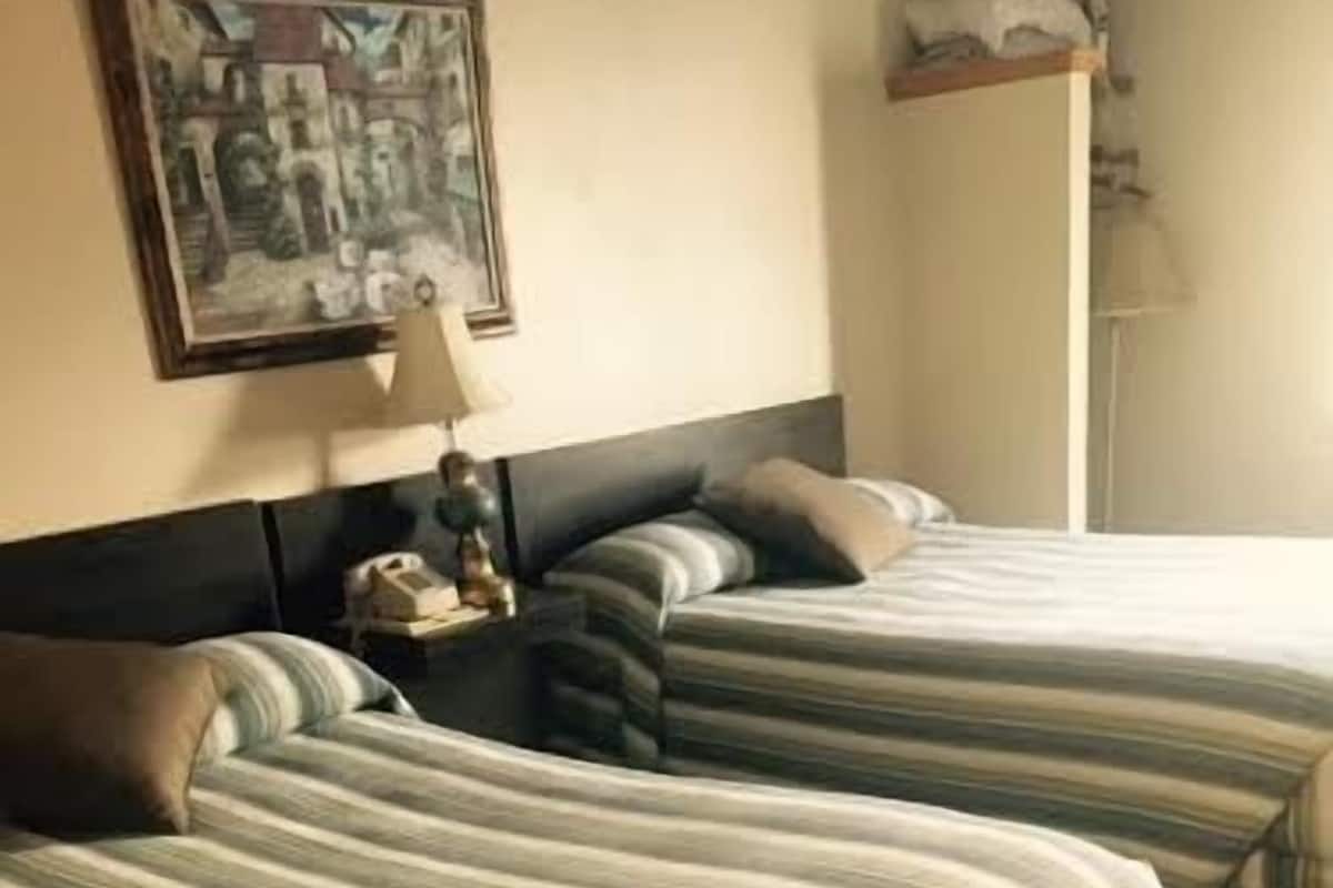 A hotel room with two beds, a nightstand, a lamp, and a framed picture on the wall.