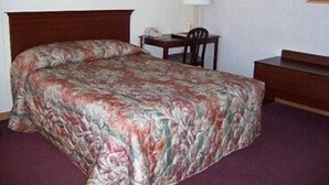 A single bed with a floral bedspread, a nightstand, a desk with a chair, and a lamp.