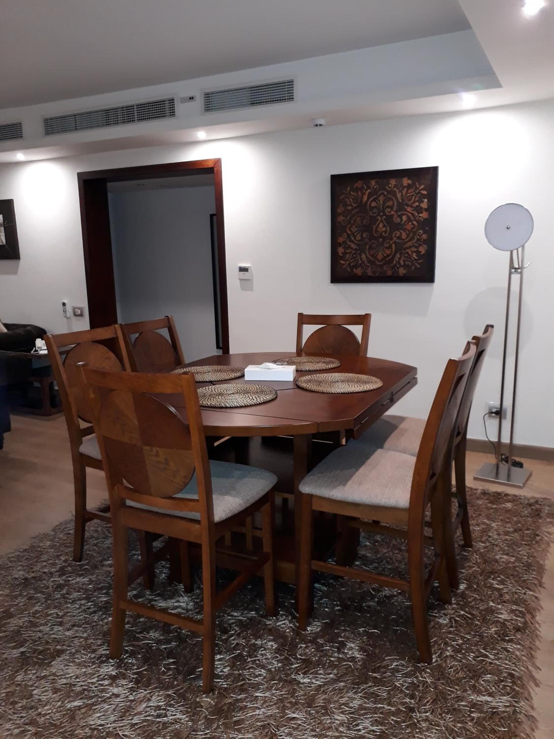 Un comedor con una mesa redonda de madera, seis sillas y un tapete decorativo.