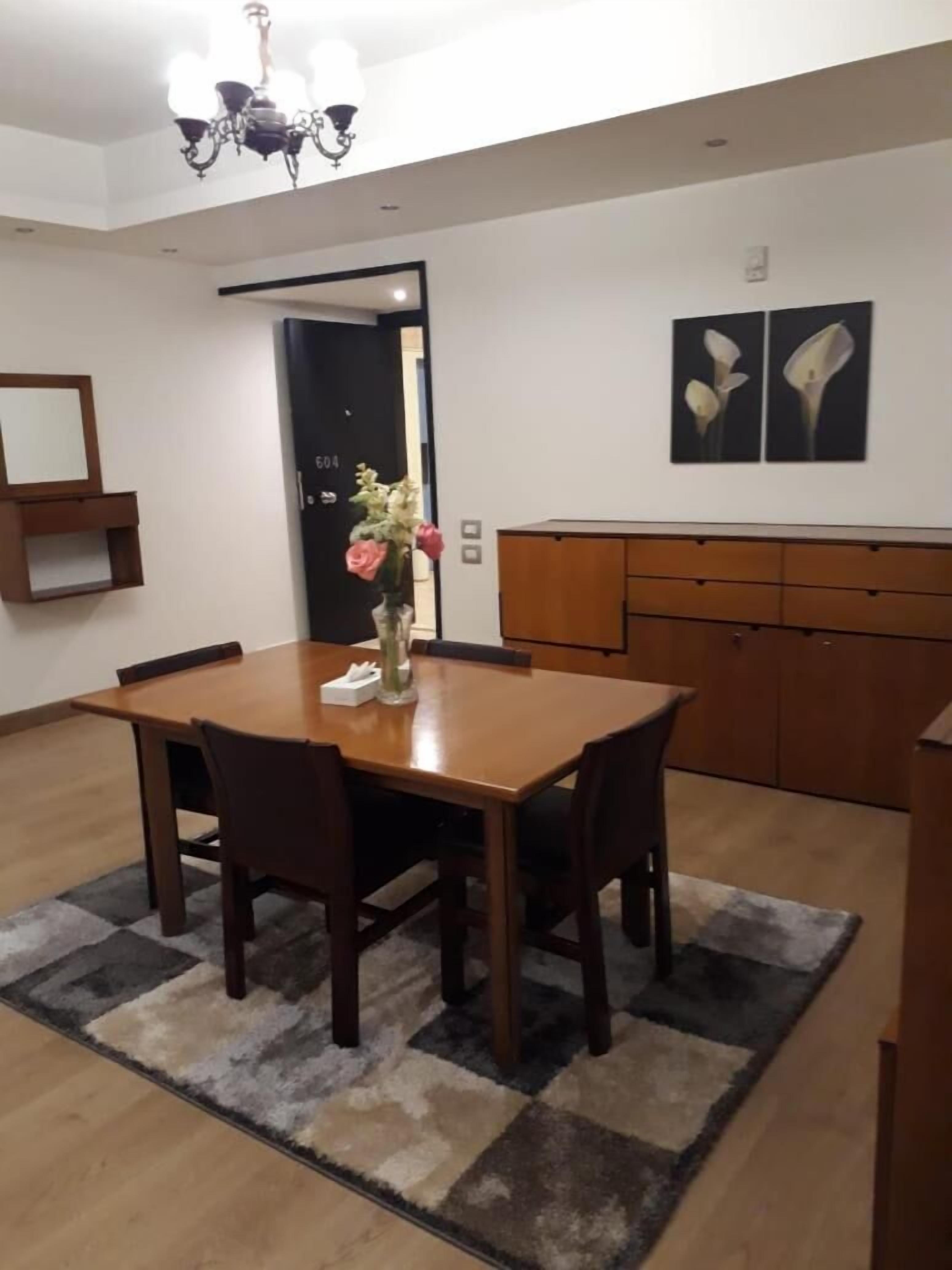 A dining area with a wooden table and chairs, a vase with flowers, a chandelier, and a door with a number on it.