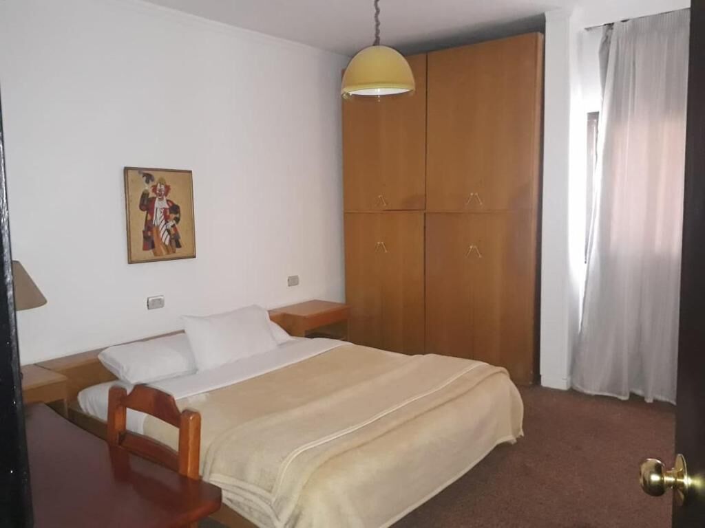 Een slaapkamer met een bed, een houten garderobe, een hanglamp en een schilderij aan de muur.