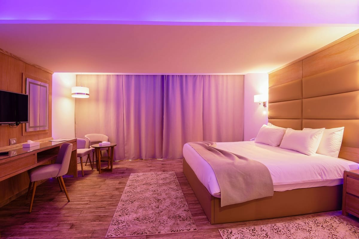 Hotellihuone, jossa on sänky, työpöytä, tuoli, televisio ja verhot.