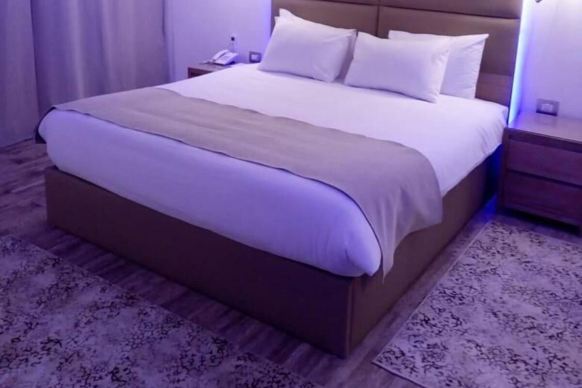 Moderni hotellihuone, jossa on suuri sänky, puinen pääty ja kuvioitu matto.
