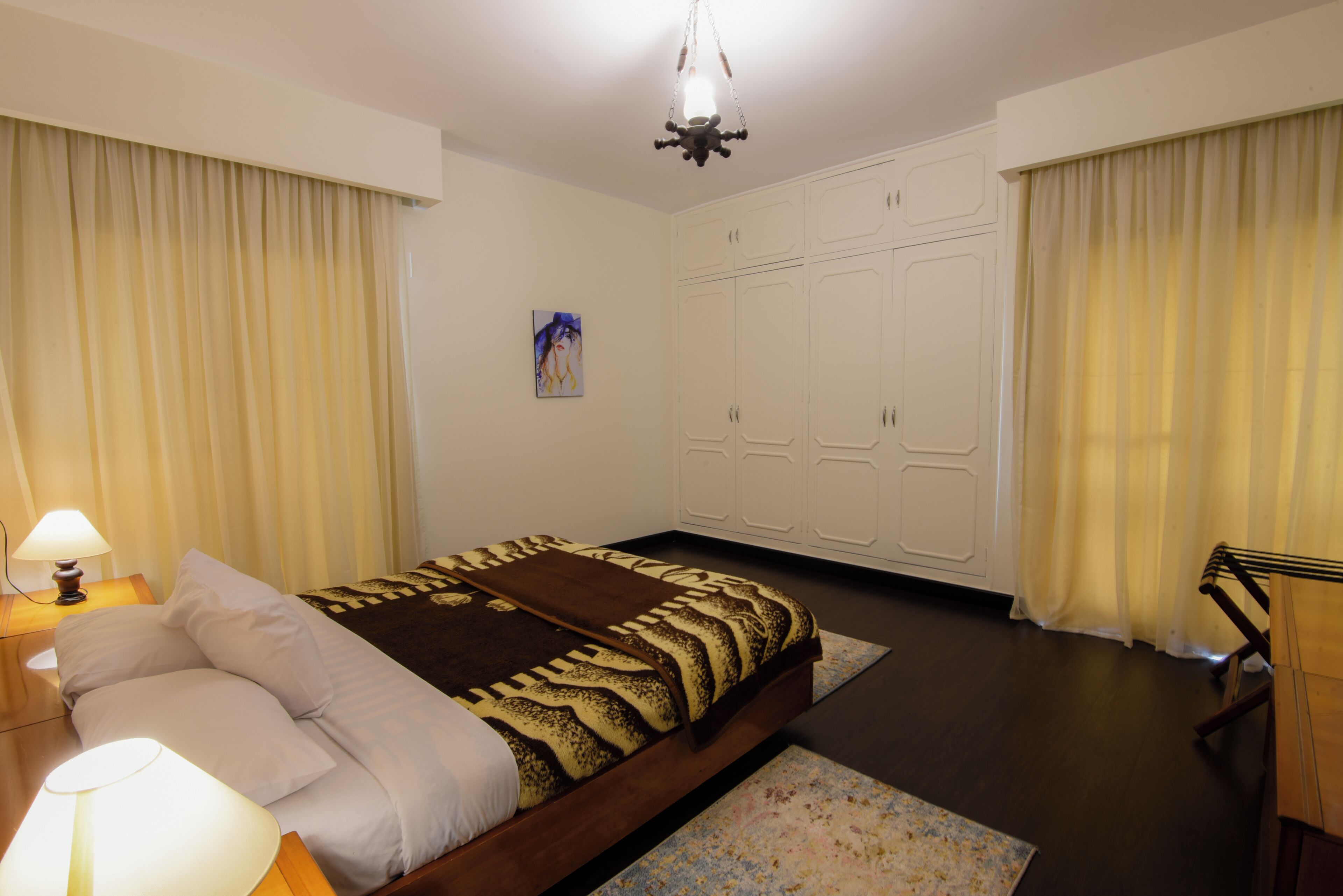 A bedroom with a bed, bedside lamps, a wardrobe, and curtains.