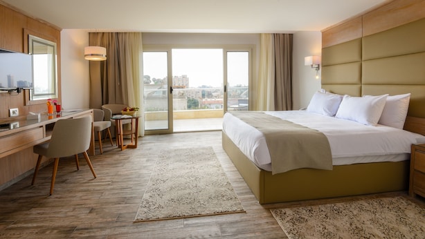 Una habitación de hotel con cama, escritorio, silla y vista a la ciudad a través de amplios ventanales.