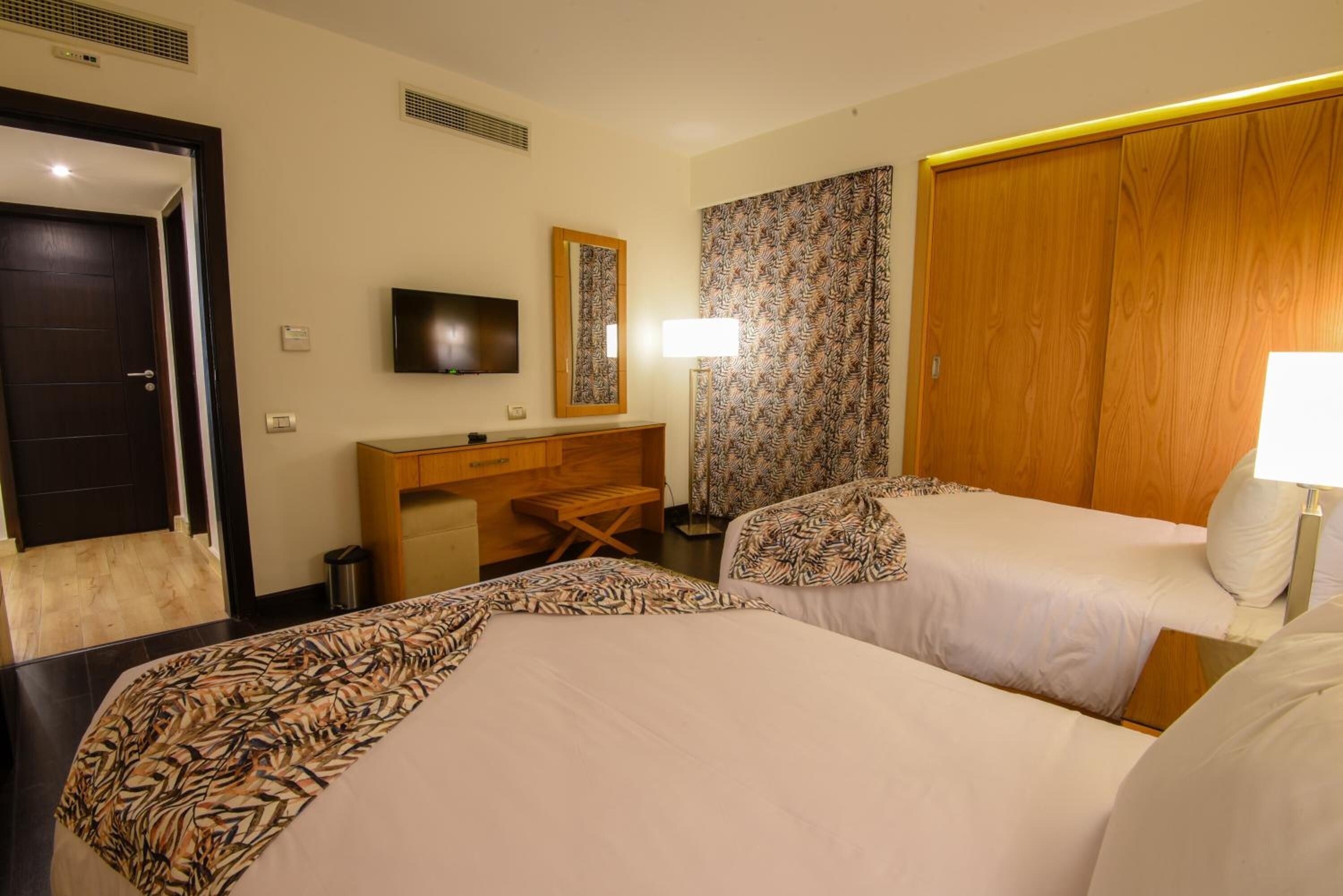A hotel room with two beds, a desk, a television, and a wardrobe.
