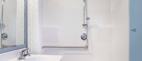 A bathroom with a white sink, a mirror, a shower with a handheld showerhead, and a grab bar.