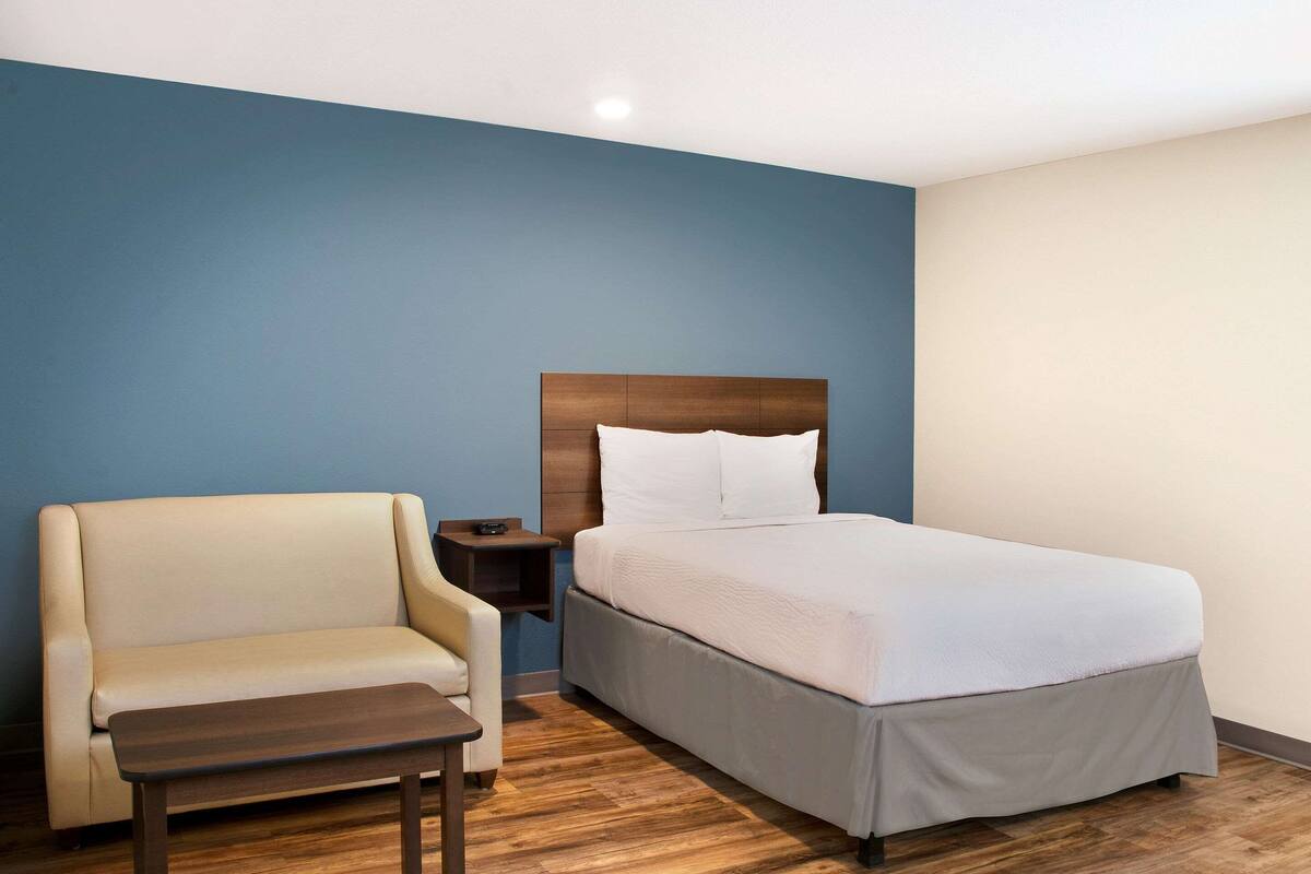 Une chambre d’hôtel avec un lit, une chaise, une petite table et une table de chevet.
