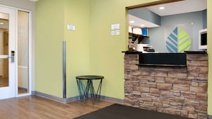 Un espace d’accueil avec un mur en pierre, une petite table ronde et un comptoir de réception.