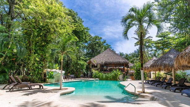 A pool area with lounge chairs, a thatched-roof structure, and lush greenery. - Banana Beach Hotel (Cóbano)