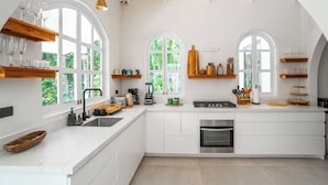 A spacious kitchen with white cabinetry, large windows, and a central island. - Banana Beach Hotel (Cóbano)